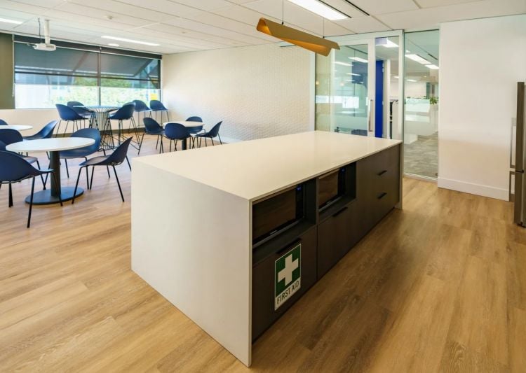 Office area with a large white island featuring under-counter storage and a first aid kit, with blue chairs and tables in the background