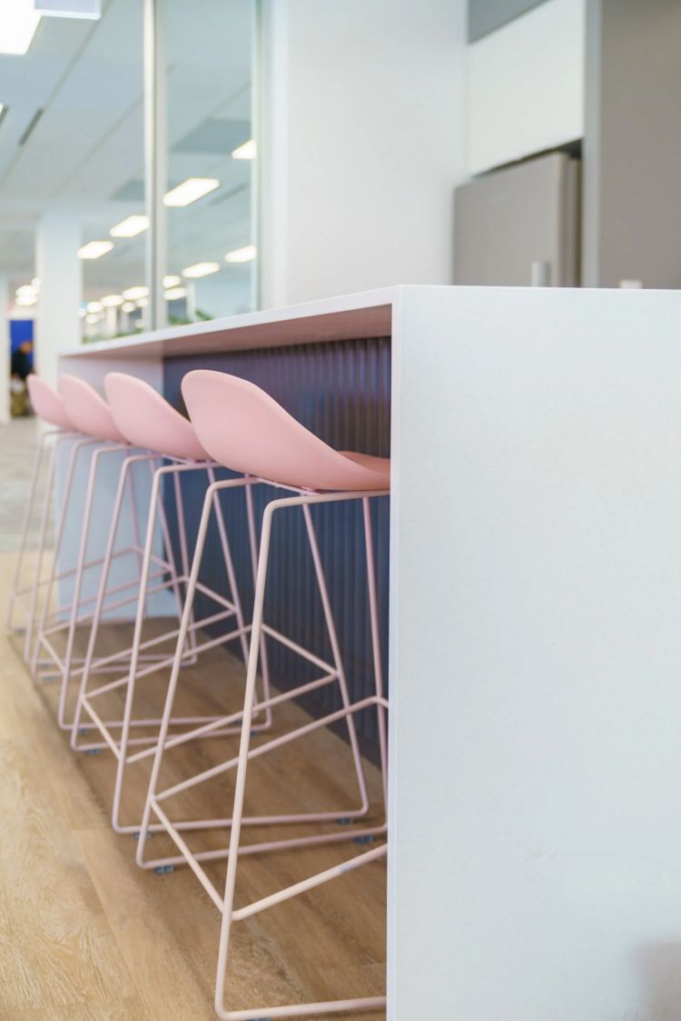 Side view of a white counter with pink chairs and metallic legs in an office setting
