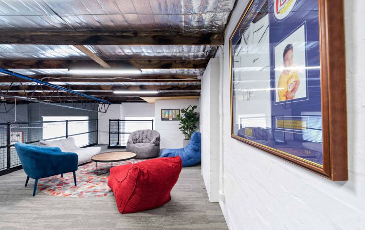 Cozy office lounge with colorful armchairs, a beanbag, and exposed ceiling beams, featuring a framed photo on the wall.