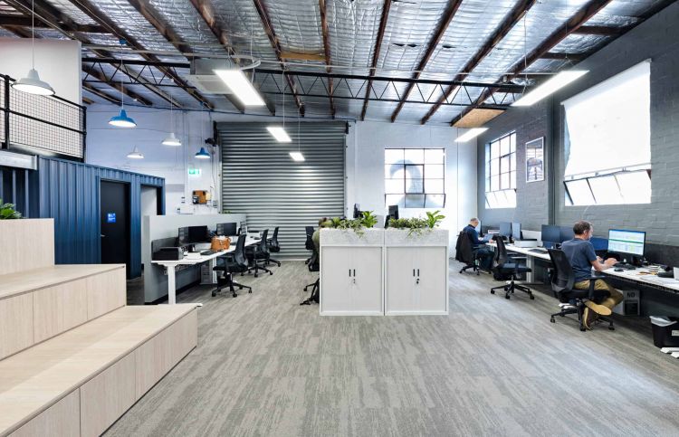Industrial office workspace with exposed beams, multiple workstations, and bright natural light.