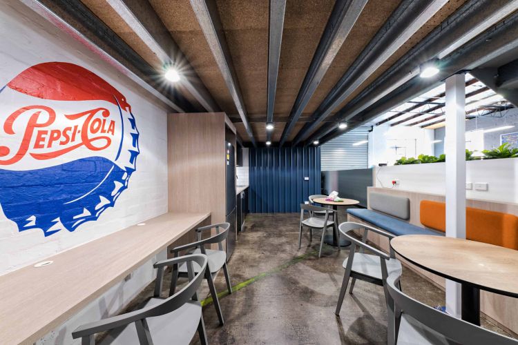 Casual office break area with a vintage Pepsi-Cola mural, modern seating, and industrial ceiling details.