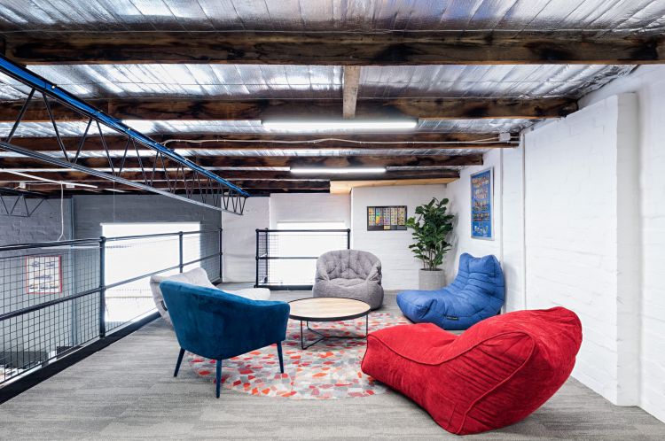 Cozy office lounge area with colorful chairs, a red beanbag, and industrial ceiling elements.