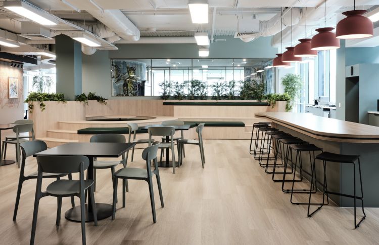 A modern office break room with sleek furniture, plant decor, and pendant lighting.