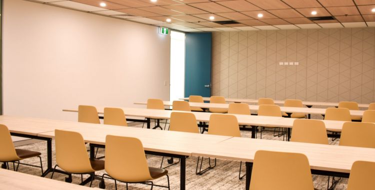  Spacious meeting room with wooden tables, mustard-colored chairs on a patterned carpet