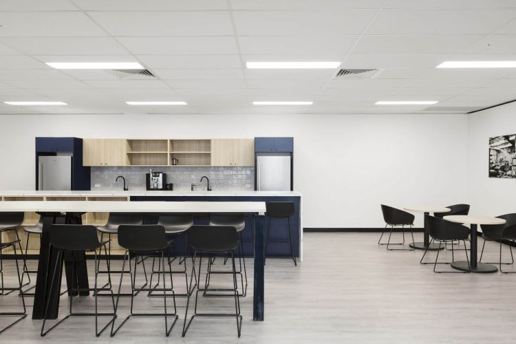 A similar view of the office kitchenette with wooden shelving and a communal table with chairs.