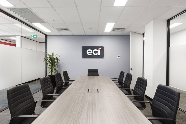 A modern boardroom with a long wooden table, surrounded by black chairs, and a 'eci' logo on the wall.