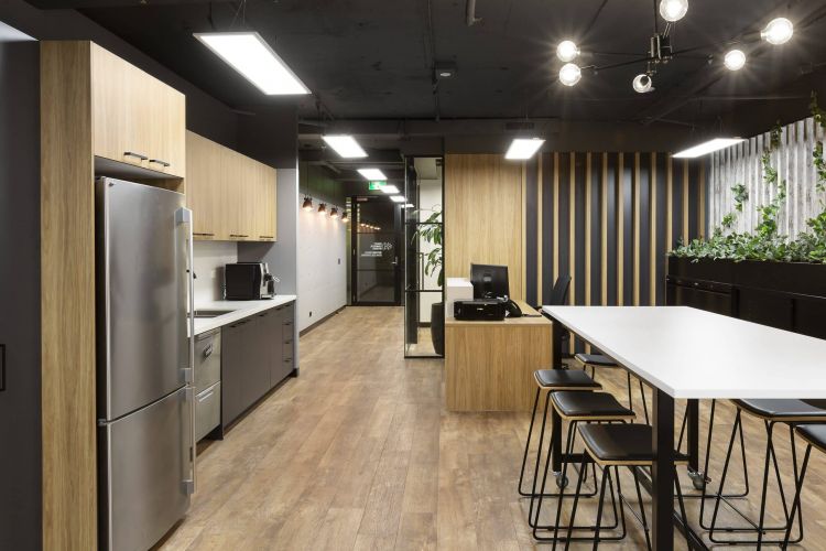 A kitchen space in an office with stainless steel appliances, wooden cabinets, and a high table with black stools.