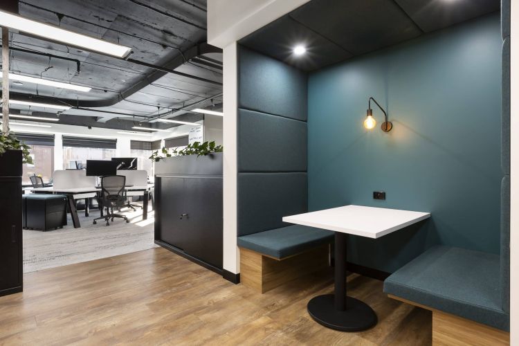 A cozy nook with blue booth seating, a white table, and elegant wall lighting in an office setting.