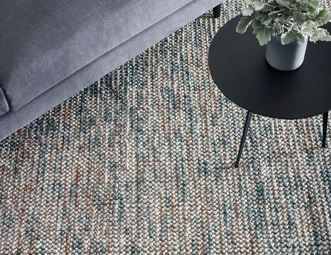 Magic Rug in Oasis. Textured wool rug in neutral cream, blue and brown tones with blue sofa.