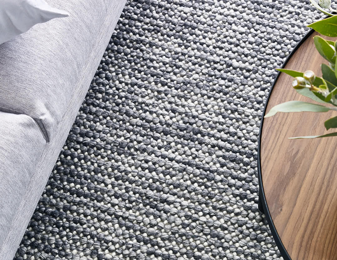 Magic Rug in Storm. Textured wool rug in neutral grey and dark tones with natural coffee table.