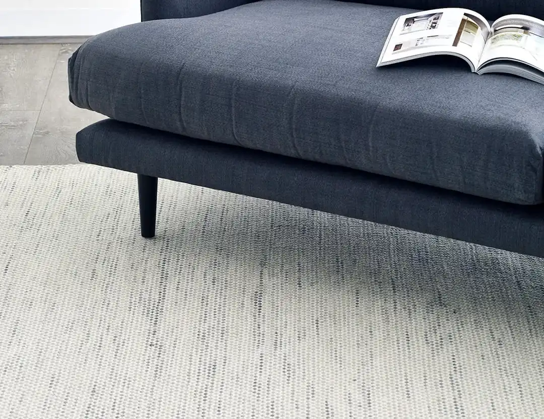 Subi Wool Rug Silver Ivory. Detailed image of low profile flatweave rug in light grey with cream marle and blue couch
