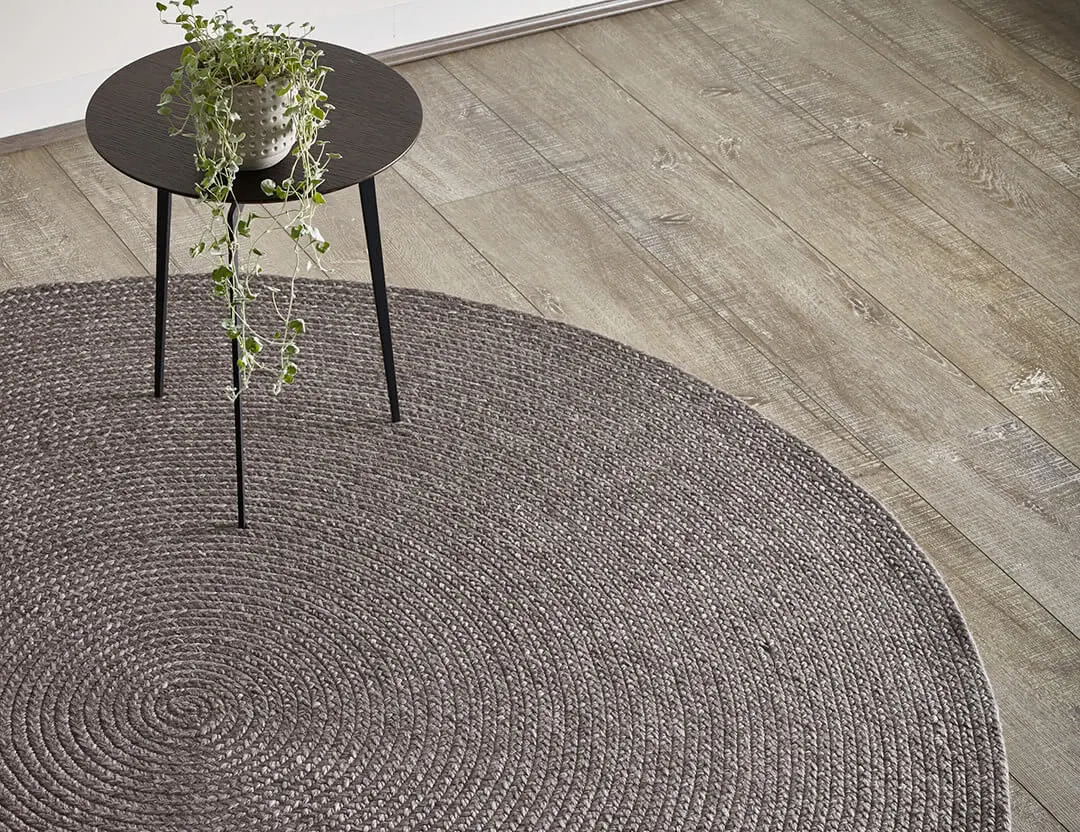Paddington round wool rug in brown charcoal with a black side table and pot plant
