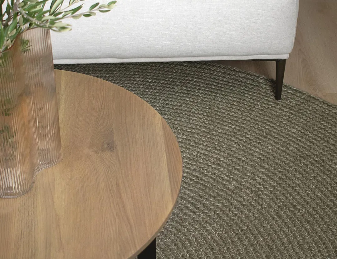 Paddington round wool rug in olive green with a wooden side table and white chair