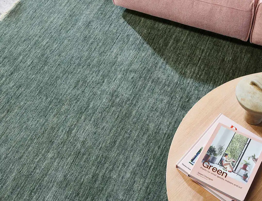 Diva Fringed Wool Rug in lillypad green with blush pink sofa and timber coffee table with a stack of books