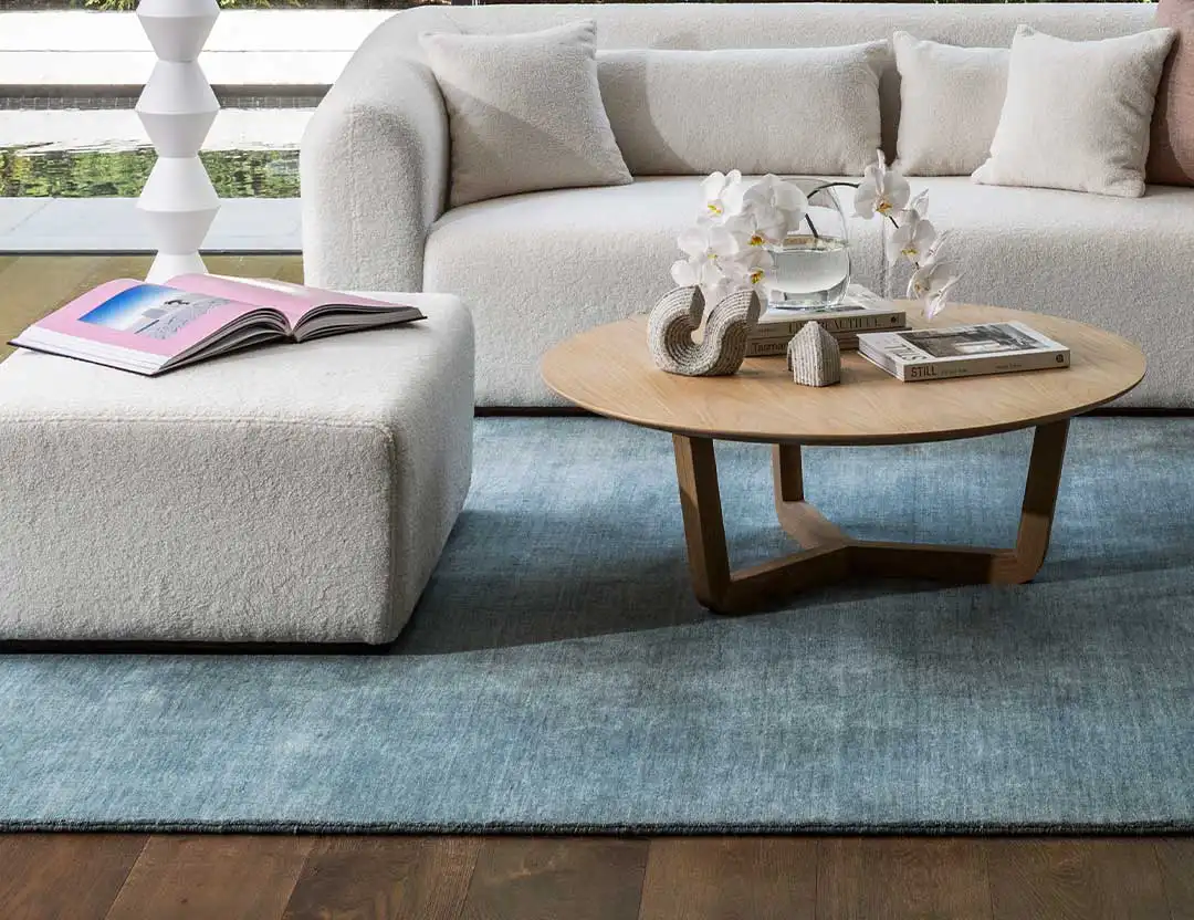 Diva Fringed Wool Rug in Sky Blue in loungeroom setting with rounded wooden coffee table and beige lounge