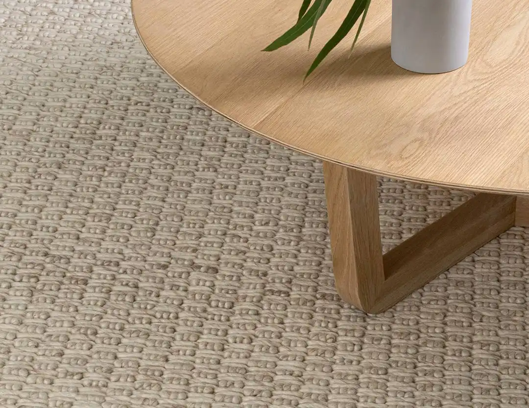 Marco Wool Rug in Linen beige with an oak coffee table and pot plant