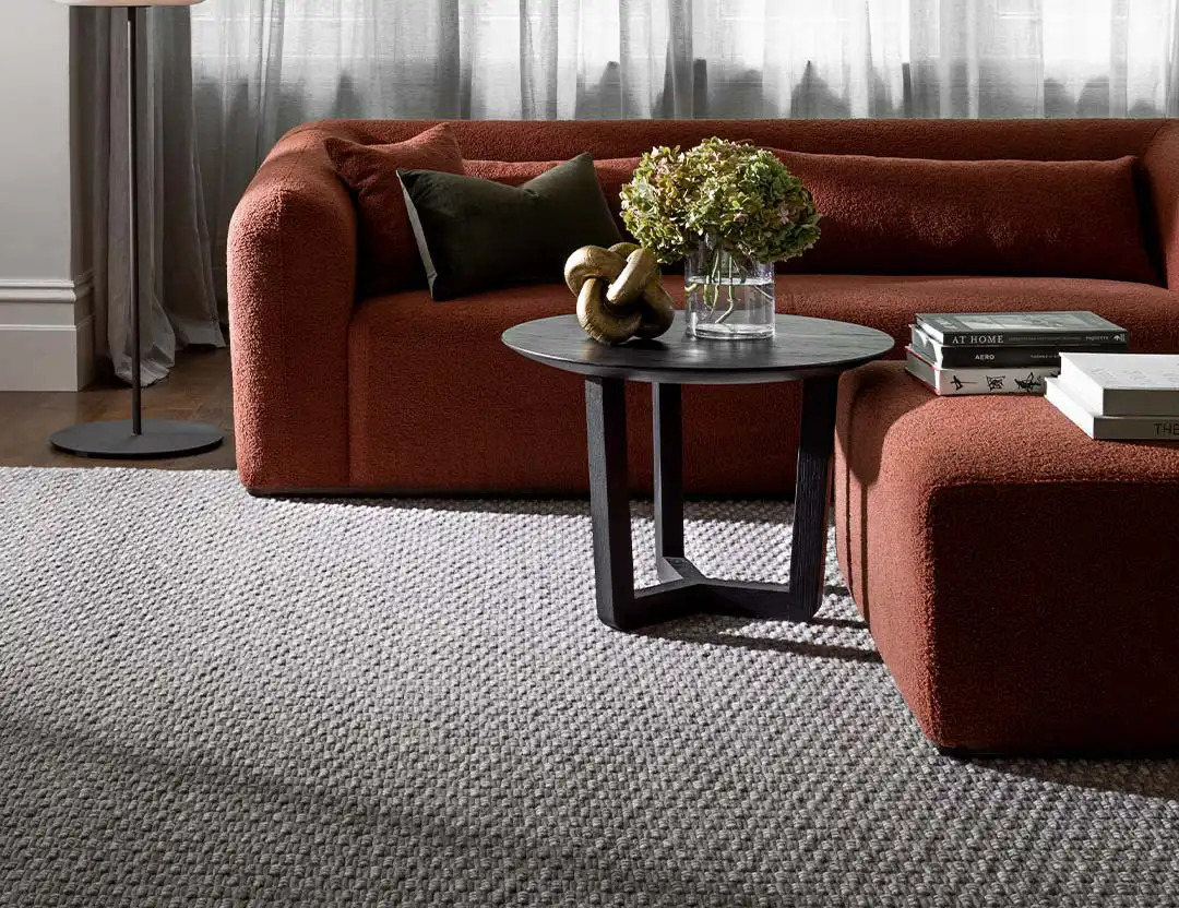 Marco Wool Rug in Ice beige with a brown rust sofa, matching ottoman, and black coffee table
