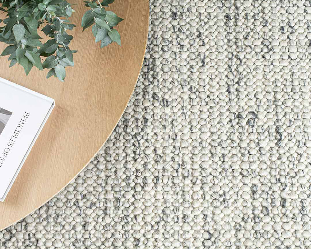 Magic Rug in Ice. Textured wool rug in neutral cream and dark tones with natural coffee table.
