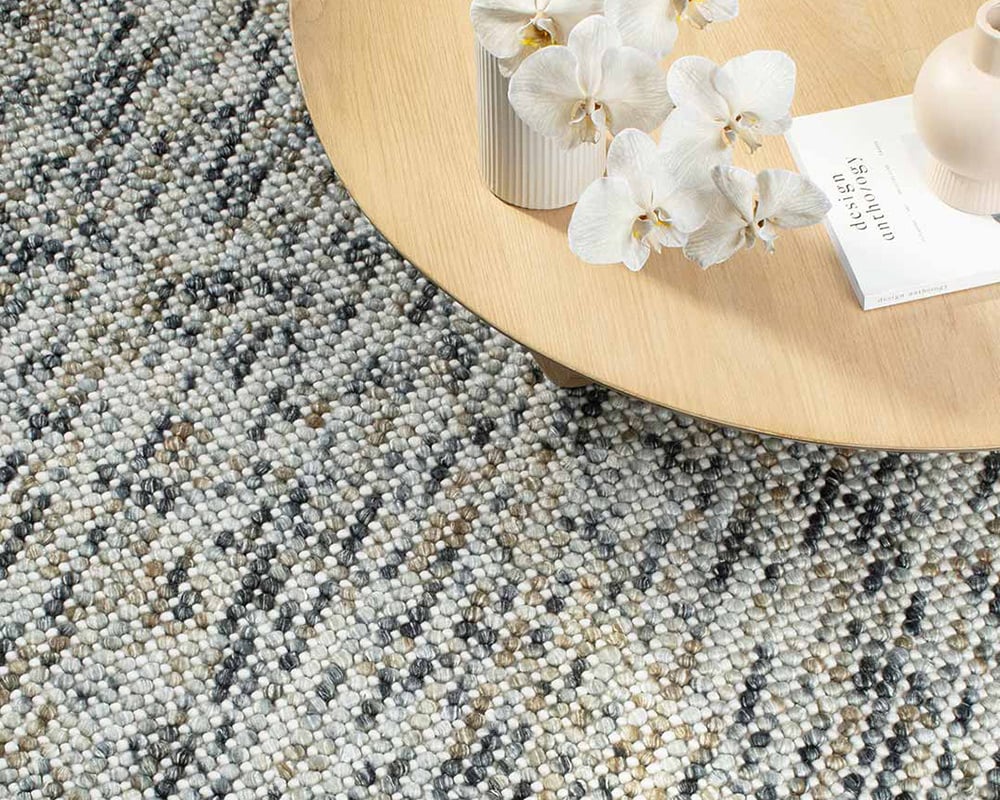 Magic Rug in Mineral. Textured wool rug in neutral cream, blue and brown tones with natural coffee table.