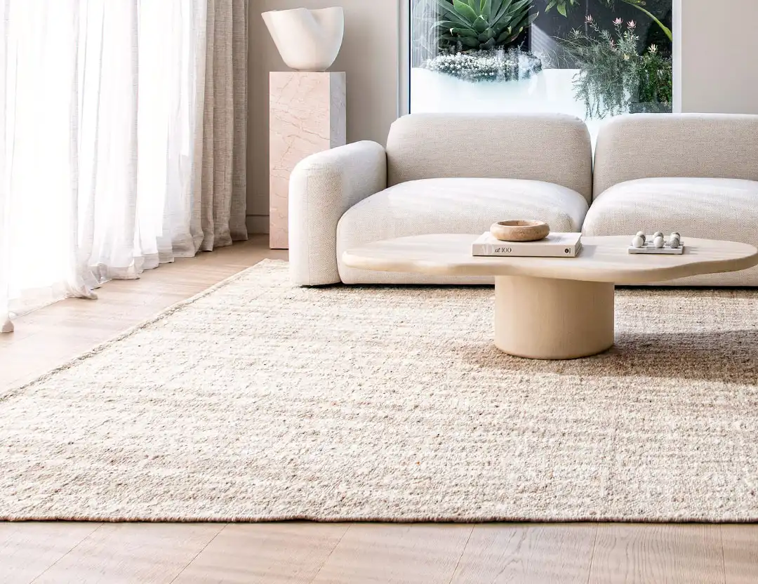 Kasbah Wool Rug in Ivory & Sand beige in sunlit open plan room with beige sofa, oak coffee table, & sculpture stand