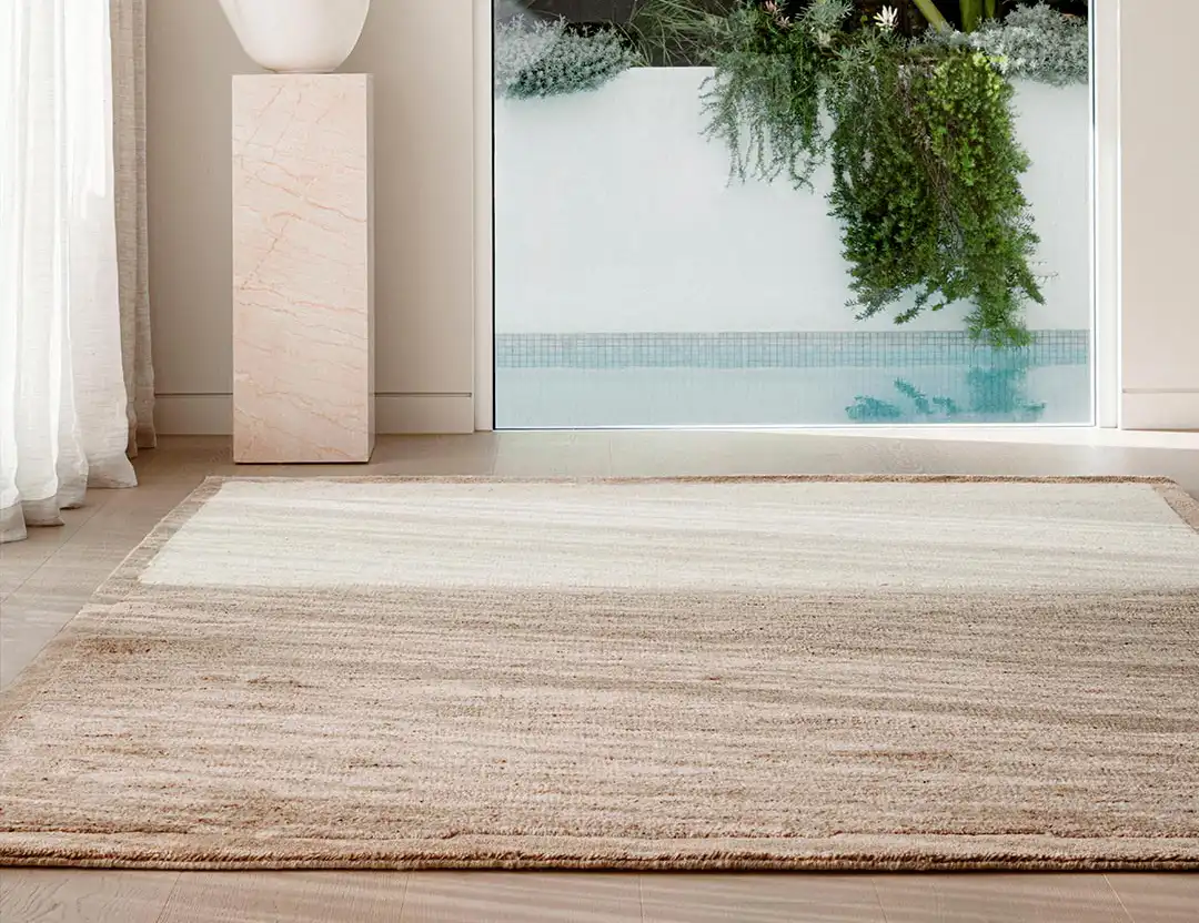 Tessera Wool Two-Toned Rug natural beige in sunlit room by a pool and sculpture