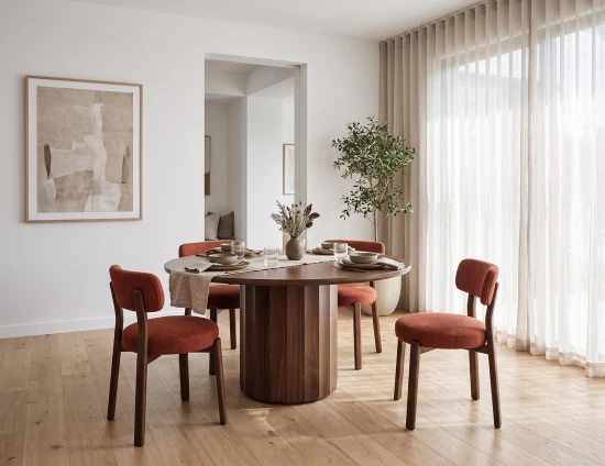 round wooden dining table with burnt orange dining chairs in a dining room with sheer curtains