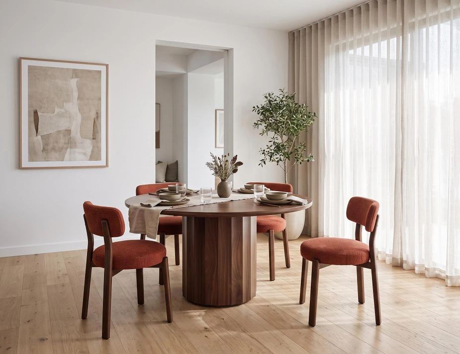 round wooden dining table with burnt orange dining chairs in a dining room with sheer curtains